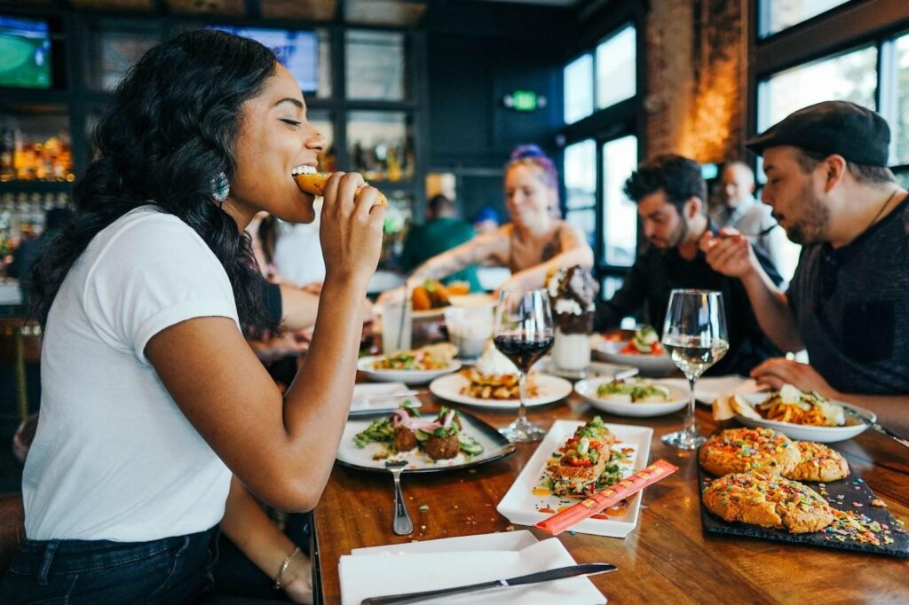 girl eating pizza, food in table, wine glass, group of people, bokeh, restaurant